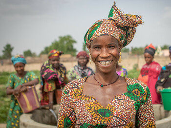 Eine Frau mit buntem Kleid und Kopftuch steht vor einem Bewässerungsbrunnen in der Region Kayes in Mali.