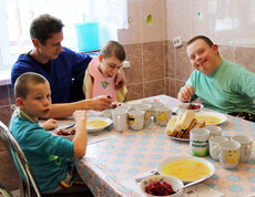 Kinder im Kinderdorf Gomel nehmen gemeinsam mit einem Betreuer ihre Mahlzeiten ein, wobei einige Kinder unterstützt werden.