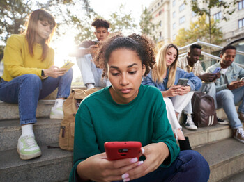 Eine Gruppe junger Menschen sitzt in einer Stadt auf einer Treppe. Alle schauen fokussiert auf ihr Smartphone.