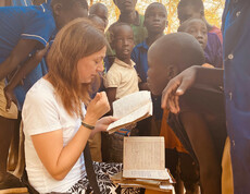 Die Bereichsleiterin Alexandra Blattnig-Rull der Auslandshilfe der Caritas Kärnten sitzt bei einem Projektbesuch umringt von Kindern der Schule und fragt diese wie es ihnen geht.