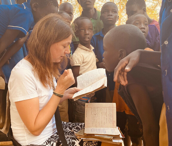 Die Bereichsleiterin Alexandra Blattnig-Rull der Auslandshilfe der Caritas Kärnten sitzt bei einem Projektbesuch umringt von Kindern der Schule und fragt diese wie es ihnen geht.