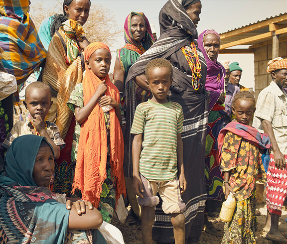 Eine Gruppe afrikanischer Kinder und Erwachsener warten auf die Verteilung von Lebenmitteln.