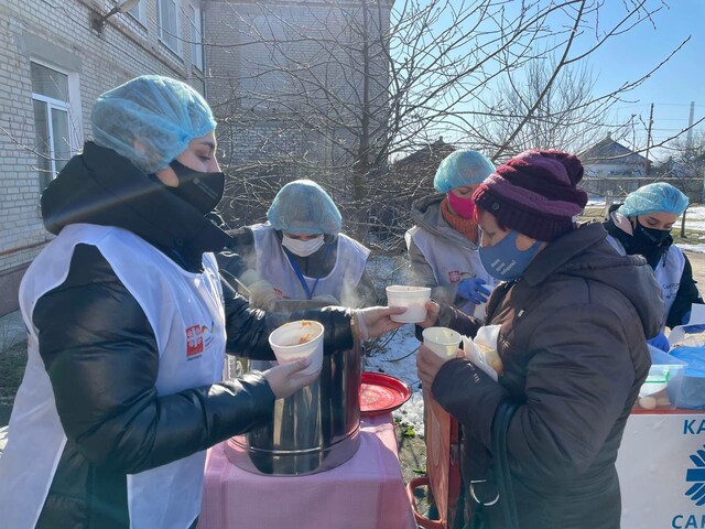 Caritas-Team beim Austeilen von Suppe, im Bild eine Dame, die gerade eine Suppe von einer Caritas-Kollegin entgegennimmt