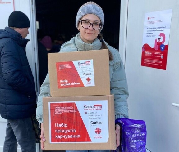 Eine Frau in winterlicher Kleidung hält zwei Pakete auf dem Arm