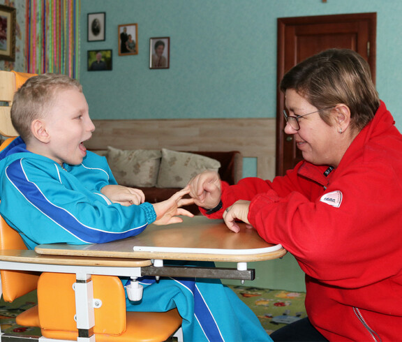 Eine Betreuerin spielt mit einem Kind im Kinderdorf Gomel und unterstützt es bei einer interaktiven Aktivität.