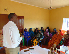 Frauen des Ortes Kinisa in Kenia sitzen in einem Gemeindegebäude und hören dem Projektleiter bei der Schulung zu.