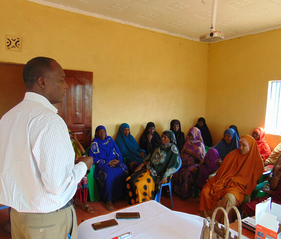 Frauen des Ortes Kinisa in Kenia sitzen in einem Gemeindegebäude und hören dem Projektleiter bei der Schulung zu.