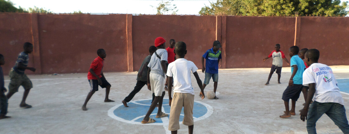 Viele Kinder beim Fußball spielen auf einem Fußballfeld aus Beton.