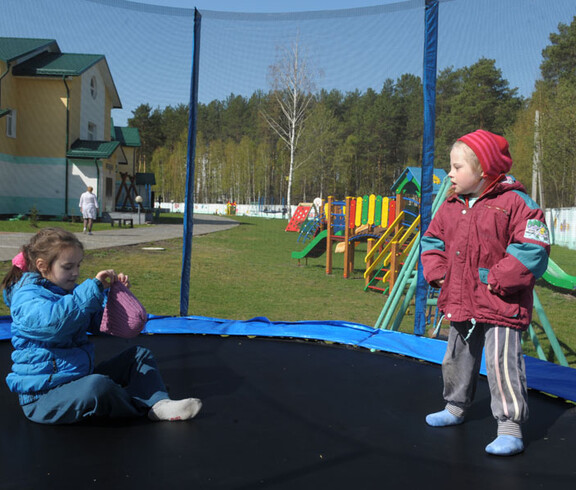 Kinder spielen auf dem Spielplatz im Kinderdorf Gomel, umgeben von Spielgeräten und einer sicheren Umgebung.