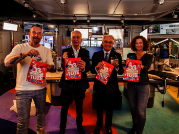 Vier Personen stehen in einem Radiostudio, alle haben eine bunte Tüte, die Ö3-Wundertüte, in der Hand und geben gerade ein Handy hinein. Die Personen stehen nebeneinander und schauen in die Kamera