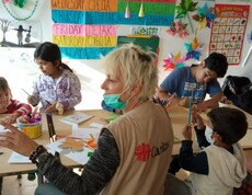 Kinder sitzen rund um einen Tisch und basteln, eine Caritas-Mitarbeiterin sitzt bei ihnen.