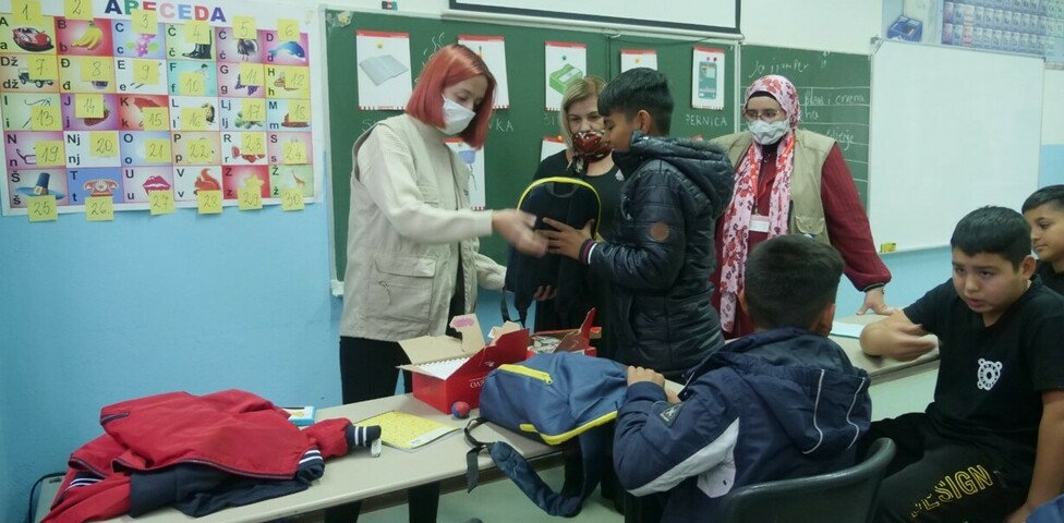 Kinder in einem Klassenraum, mit ihnen sind zwei erwachsene Frauen. 