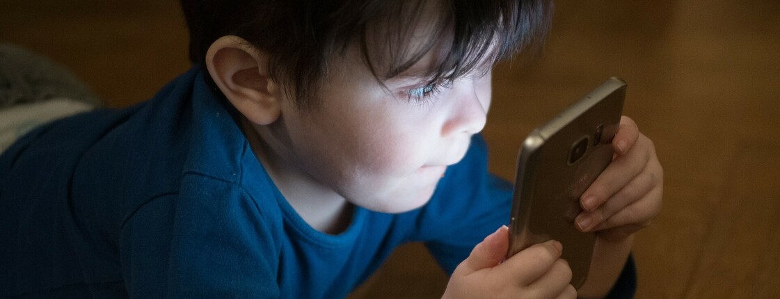 Man sieht einen Bub, er hält ein Handy in der Hand und schaut hinein.