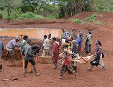 Eine Gruppe von Menschen in Afrika gräbt ein Regenwasser-Sammelbecken.