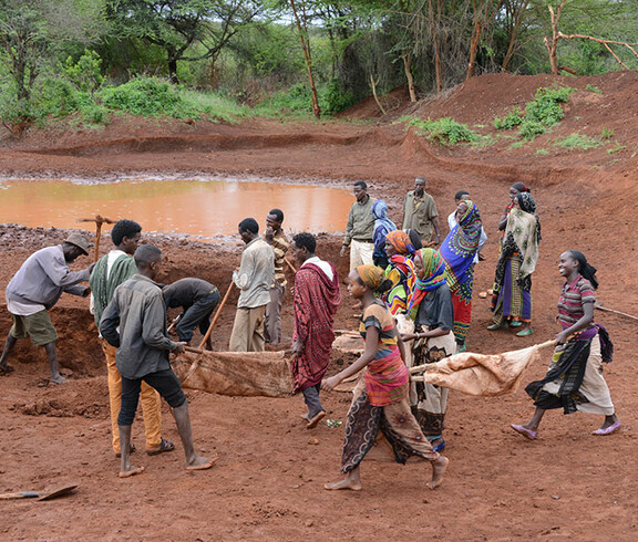 Eine Gruppe von Menschen in Afrika gräbt ein Regenwasser-Sammelbecken.