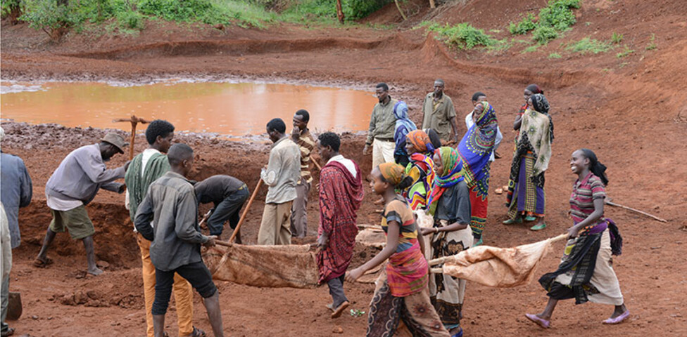 Eine Gruppe von Menschen in Afrika gräbt ein Regenwasser-Sammelbecken.