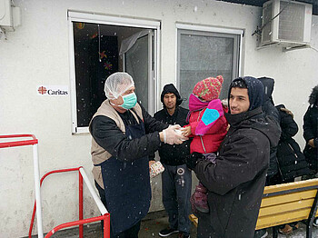 Ein Caritas Mitarbeiter gibt ein Lebensmittelpaket an einen Flüchtling und sein Kind.