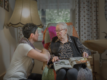 Frau spricht mit älterer Frau im Lehnstuhl